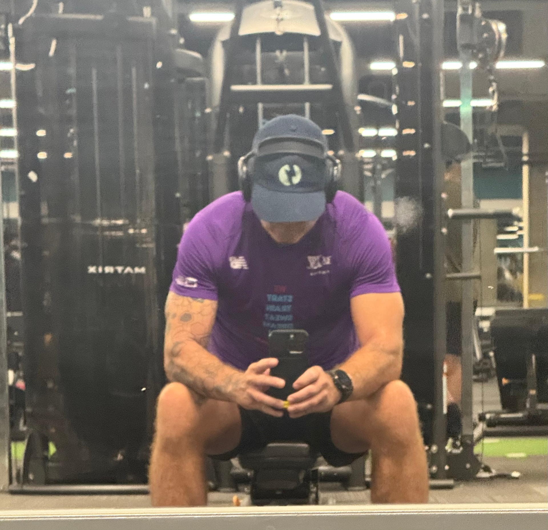 Jake sitting on a gym bench, head down, taking a mirror selfie